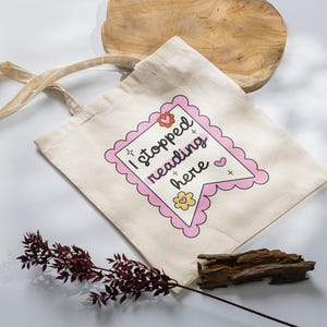K&ouml;nnte beinhalten: Eine beige Tragetasche mit einem rosa und wei&szlig;en Banner, auf dem "Ich habe hier mit dem Lesen aufgeh&ouml;rt" steht, mit Herzen und Sternen.