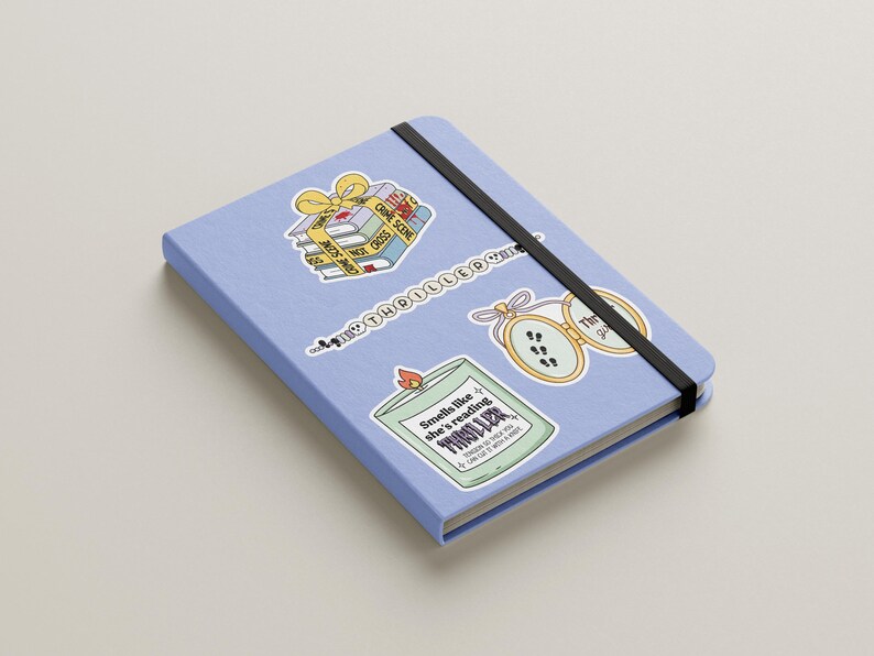 May include: A blue notebook with three stickers. One sticker is of a stack of books with a yellow ribbon and the text "Crime Scene Do Not Cross". Another sticker is of a candle with the text "Smells like she's reading a thriller". The third sticker is of a locket with the text "The Girl on the Train".
