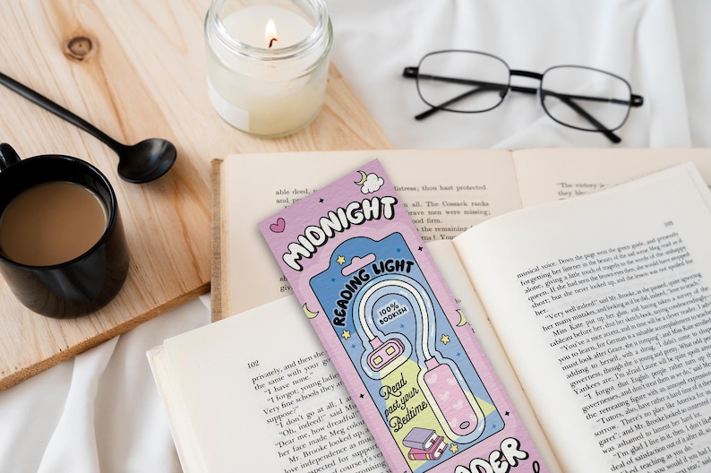 Puede incluir: Un marcap&aacute;ginas rosa y azul con una ilustraci&oacute;n de dibujos animados de una luz de lectura. El marcap&aacute;ginas dice "Midnight Reading Light" y "100% Bookish".