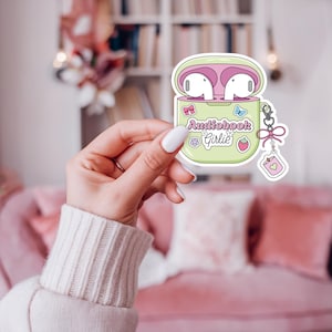 May include: A sticker featuring a cartoon illustration of a light green AirPod case with pink interior and white AirPods. The case has the text "Audiobook Girlie" and decorative elements like a bow, butterfly, flower, and strawberry.