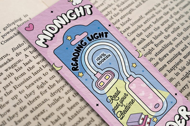 Puede incluir: Un marcap&aacute;ginas rosa y azul con una luz de lectura blanca adjunta. El marcap&aacute;ginas tiene una luna creciente, estrellas y el texto "MIDNIGHT READING LIGHT 100% BOOKISH". El texto "Read past your Bedtime" est&aacute; en la luz.
