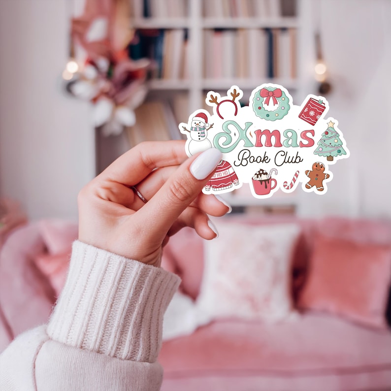 May include: A colorful sticker with the text "Xmas Book Club" and festive illustrations. The design includes a snowman, a wreath, a gift, a Christmas tree, a sweater, a mug of hot chocolate, a candy cane, and a gingerbread person.