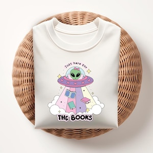May include: White t-shirt with a graphic of a green alien in a flying saucer with the text "Just here for the books".