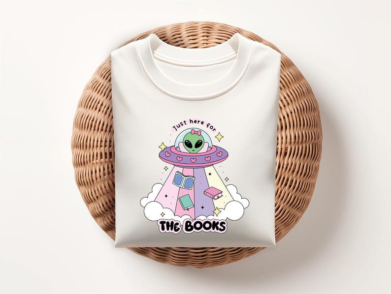 May include: White t-shirt with a graphic of a green alien in a flying saucer with the text "Just here for the books".