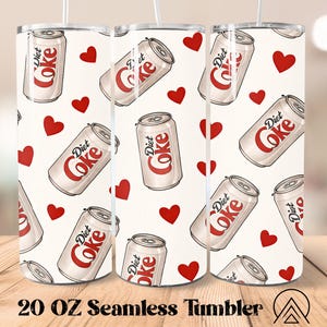 May include: A 591 ml seamless tumbler with a repeating pattern of Diet Coke cans and red hearts on a cream background. The Diet Coke cans are white with red text. The tumbler has a white straw.