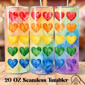 May include: Three 20 oz seamless tumblers with a rainbow heart design. Each tumbler features a watercolor effect with red, orange, yellow, green, blue, and purple hearts. The tumblers have a gold glitter effect and the text "20 OZ Seamless Tumbler".