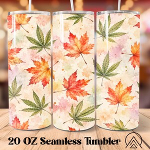 May include: A 20 oz cylindrical tumbler featuring a watercolor pattern of orange and red maple leaves interspersed with green cannabis leaves on a cream background. The design includes a white straw and the text 20 OZ Seamless Tumbler.