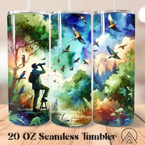 Könnte beinhalten: Ein 20 oz Edelstahlbecher mit einem Aquarelldesign einer Waldszene mit Vögeln, die am Himmel fliegen. Eine Person steht im Wald und schaut durch ein Fernglas. Der Becher ist nahtlos und wird mit einem Strohhalm geliefert.