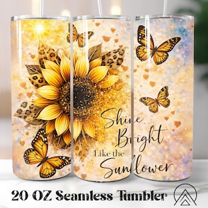 May include: A 20 oz seamless tumbler featuring a vibrant sunflower design with butterflies and leopard print accents. The tumbler has the text "Shine Bright Like the Sunflower" and is decorated with hearts.