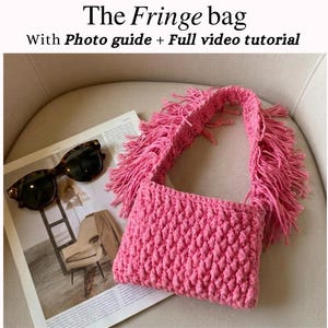 Può includere: Una borsa rosa con frange, con un corpo strutturato e una lunga tracolla con frange. La borsa è appoggiata su una rivista accanto a occhiali da sole. Il testo sull'immagine recita "The Fringe bag With Photo guide + Full video tutorial."