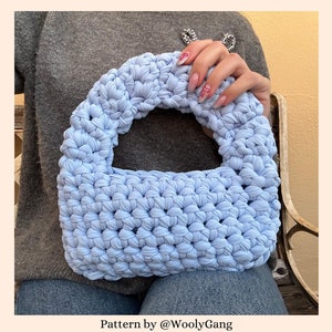 May include: A light blue crocheted bag with a round handle. The bag is made with a textured stitch and has a slightly slouchy shape. Pattern by @WoolyGang