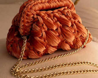 Könnte beinhalten: Eine gehäkelte Handtasche mit einer goldenen Kettenkette. Die Tasche ist aus einem weichen, orangefarbenen Stoff gefertigt und hat ein einzigartiges, strukturiertes Design. Das Bild enthält den Text "CROCHET PDF PATTERN STEP BY STEP INSTRUCTIONS PHOTOS".