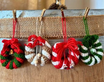 May include: Four crocheted Christmas wreath ornaments. Each wreath is a different color combination: red and green, white and brown, red and white, and green and white. Each wreath has a red, white, or green string for hanging and is decorated with a bow and small bells.