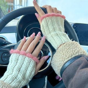 Può includere: Guanti senza dita color crema con bordo rosa a balze. I guanti sono lavorati a maglia e sembrano essere fatti di un filato morbido. I guanti vengono indossati mentre si tiene un volante nero.