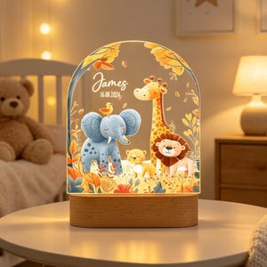May include: An arched acrylic night light with a wooden base featuring a colorful illustration of a blue elephant, a giraffe, a lion, and a small bird. The text James and 16.08.2024 is printed in white script and sans-serif font on the clear surface.