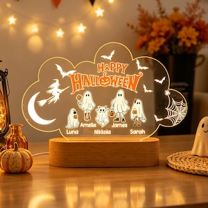 May include: A custom acrylic LED night light featuring a cloud-shaped design with the text Happy Halloween, a witch on a broom, bats, a spider web, and four ghost characters labelled with the names Luna, Amelia, Nikkola, James, and Sarah.