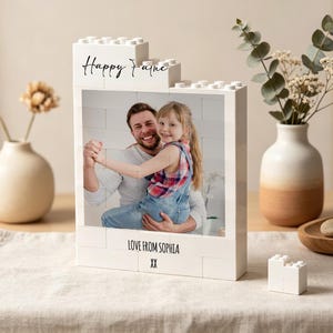 May include: A white block-style photo frame with the words "Happy Father" and "Love From Sophia XX" in black script. The frame holds a photo of a man and a child. Decorative vases and a small wooden tray are also in the image.