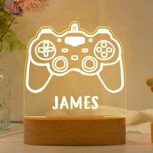 May include: A wooden base with a clear acrylic panel featuring a white outline of a video game controller. The name "JAMES" is printed below the controller.