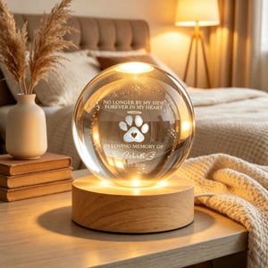 Peut inclure: Une sphère en verre transparent avec une empreinte de patte et le texte "NO LONGER BY MY SIDE FOREVER IN MY HEART" et "IN LOVING MEMORY OF Wurth B 2017-2026". La sphère repose sur une base ronde en bois éclairée. Objet décoratif.