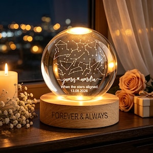Könnte beinhalten: Eine klare Glaskugellampe mit eingravierter Sternbildkarte, den Namen "james & amelia" und dem Text "When the stars aligned 13.08.2026". Die Kugel steht auf einem runden Holzsockel, in den "FOREVER & ALWAYS" eingraviert ist.
