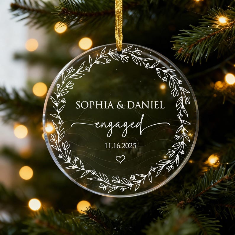 May include: Clear, round Christmas ornament with gold ribbon. The ornament features the names "Sophia & Daniel" and the word "engaged" in elegant script, along with the date "11.16.2025" and a heart symbol, surrounded by a floral wreath.