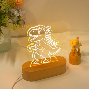May include: A wooden night light with a white dinosaur silhouette and the name "William" inscribed on the side. The light is illuminated with a warm yellow glow.
