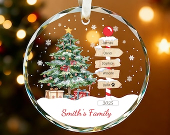 May include: A clear, round Christmas ornament with a festive design. It features a decorated Christmas tree, a signpost with names, and the text "Smith's Family" and "2025". The ornament hangs from a white ribbon.