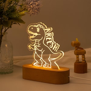 May include: A wooden night light shaped like a dinosaur with the name "Aresh" written on it. The light is on and illuminating the dinosaur.