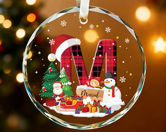 May include: A round, clear Christmas ornament with a festive design. The ornament features a large, red and black plaid letter "M" with a Santa hat. A snowman, Christmas tree, and gifts are also depicted. The name "Muriel" is written on a wooden sign.