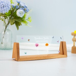May include: A wooden-based, clear acrylic sign with the text "Grandma's Garden" and "Planting Seeds of Greatness." The sign features colorful flower and butterfly graphics. The wooden base has a rectangular shape.