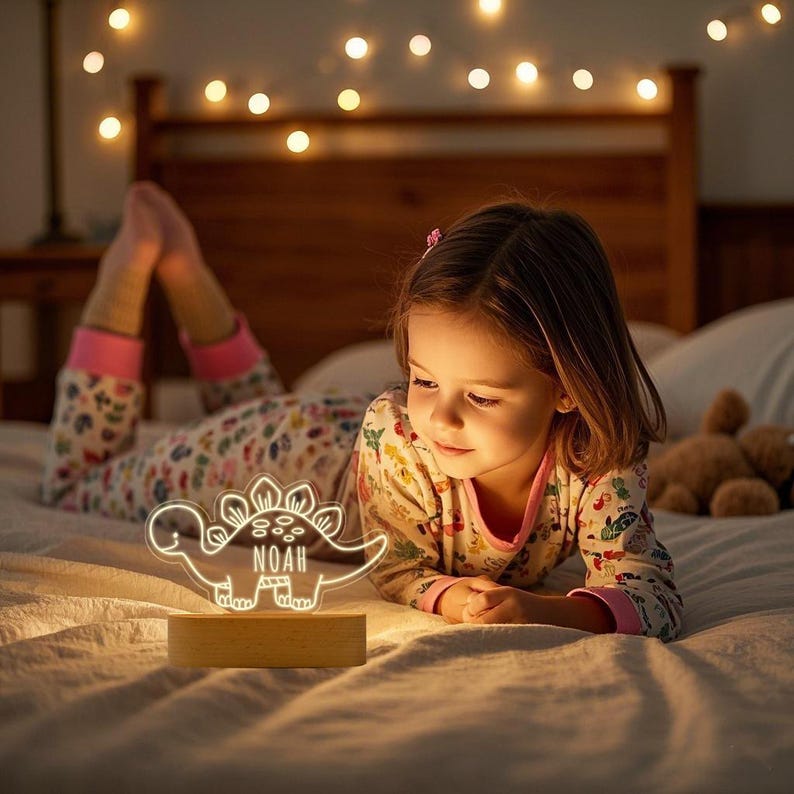 May include: A clear acrylic dinosaur-shaped night light with a light-up outline and the name NOAH etched in the centre. The lamp features a smooth, rectangular wooden base that illuminates the design with a warm, soft glow in a bedroom setting.