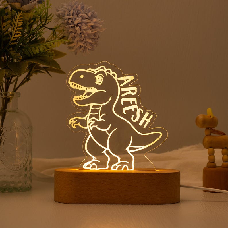 May include: A wooden night light with a dinosaur silhouette and the name "Aresh" on it. The light is on and illuminating the dinosaur.