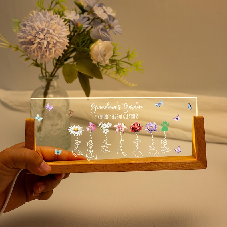 May include: A wooden-based LED light with a clear acrylic panel. The panel is illuminated with the words "Grandma's Garden" and "Planting Seeds of Greatness." It features colorful flower and butterfly graphics, and personalized names.