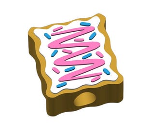 May include: A cartoon-style pastry with a brown crust, white frosting, and pink zigzag icing. Blue and pink sprinkles are scattered across the top. The pastry has a hole at the bottom, suggesting it may be a charm or pendant.