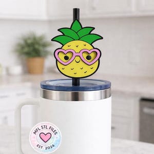 Op de afbeelding: Een witte mok met een blauw deksel en een zwart rietje, bekroond met een gele ananas met een roze hartvormige zonnebril. Een sticker op de mok leest "MFL STL FILES EST. 2024" met een hartontwerp.
