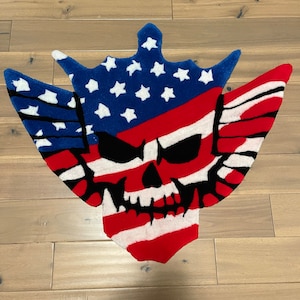Könnte beinhalten: Ein roter, weißer und blauer amerikanischer Flaggen-Teppich mit einem schwarzen Totenkopf in der Mitte. Der Teppich ist aus flauschigem Material und hat einen Used-Look.