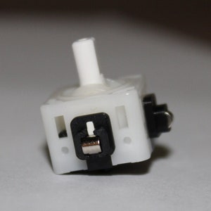 May include: A white plastic rotary switch with a black knob and two black terminals. The switch has a small white shaft extending from the top.