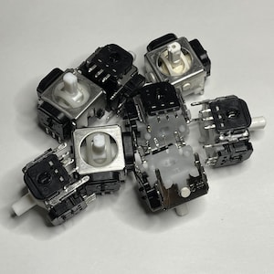 May include: A group of six black and silver analog joystick potentiometers with white plastic shafts. The potentiometers are used in video game controllers.