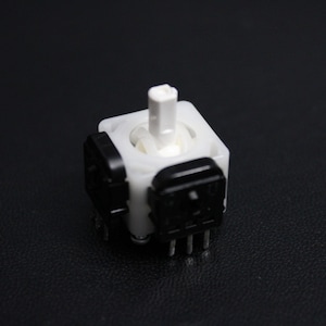 May include: A white plastic rotary encoder with a black knob and six pins. The encoder is used for controlling the rotation of a device.