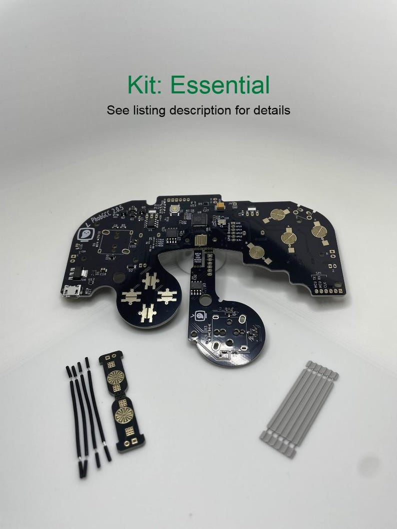 May include: A black circuit board with gold-coloured components and text that reads "PhobGCC 2.05". The board is surrounded by black and silver wires and a small black and gold button.