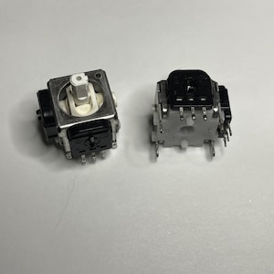 May include: Two black and silver potentiometers with multiple pins. The potentiometers are used for controlling electronic devices.