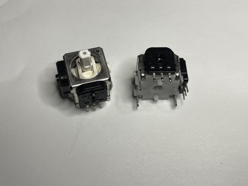 May include: Two black and silver potentiometers with multiple pins. The potentiometers are used for controlling electronic devices.