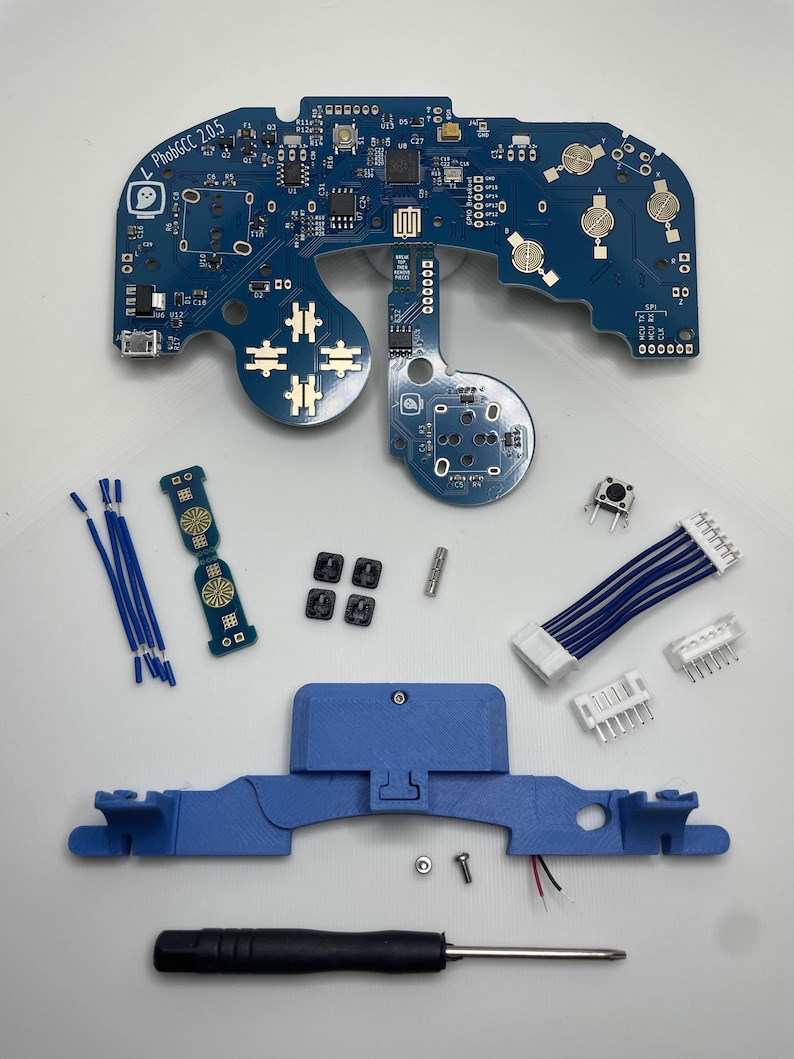 May include: A blue circuit board with the text "L PhobGCC 2.0.5" printed on it. The board is surrounded by various components, including a blue plastic case, a screwdriver, and a small blue circuit board with a circular design.
