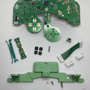 May include: A green circuit board with the text "L PhobGCC 2.0.5" printed on it. The board is surrounded by various components, including wires, buttons, and a screwdriver.