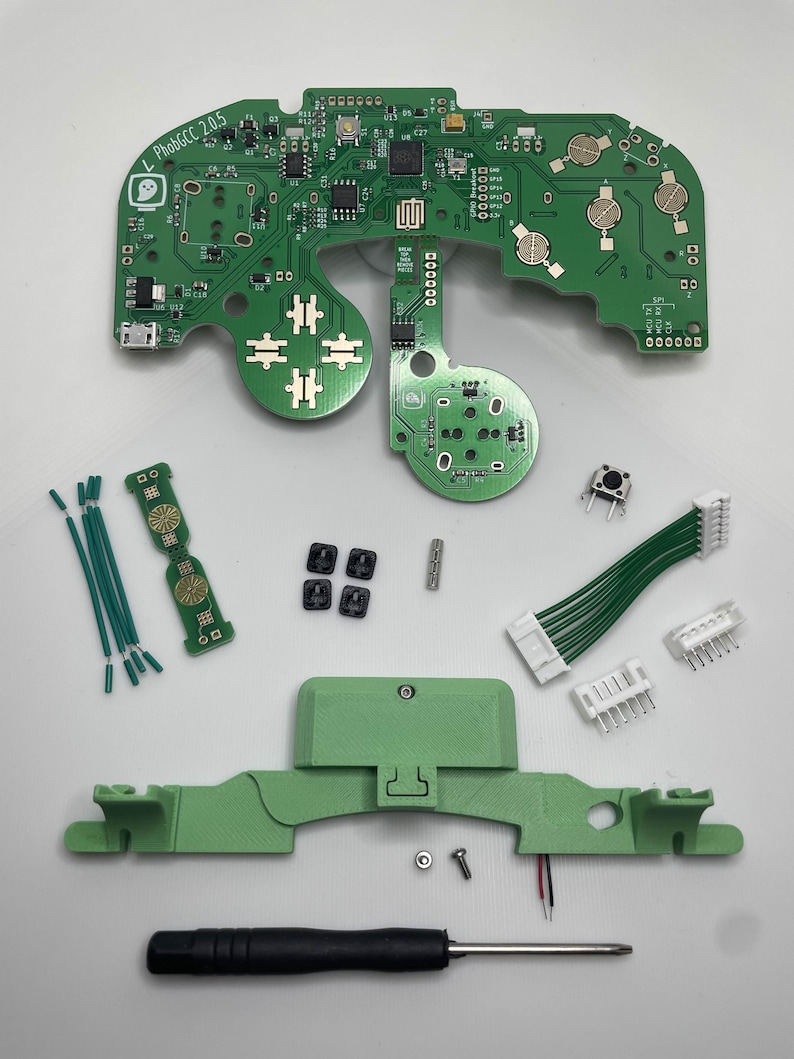 May include: A green circuit board with the text "L PhobGCC 2.0.5" printed on it. The board is surrounded by various components, including wires, buttons, and a screwdriver.