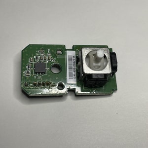 May include: A green circuit board with a small white joystick and the text "SN:2390F-68F-NS" printed on it.