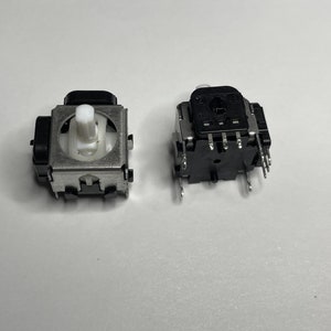 May include: Two black and silver potentiometers with white knobs. The potentiometers have multiple pins on the bottom.