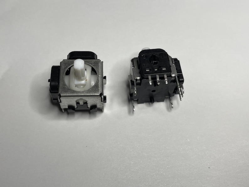 May include: Two black and silver potentiometers with white knobs. The potentiometers have multiple pins on the bottom.
