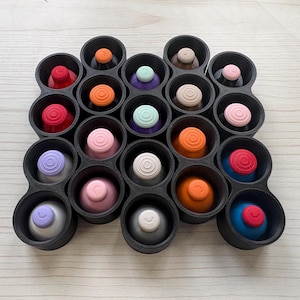 May include: A black plastic storage tray containing twenty circular compartments, each holding a colorful joystick thumbstick cover. The covers feature various solid colors including red, orange, pink, light blue, purple, white, and gray.