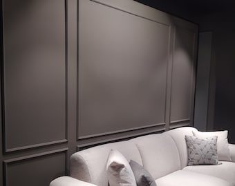 May include: A white couch with a textured fabric, featuring three pillows. The couch is positioned in front of a wall with a dark gray, paneled design.